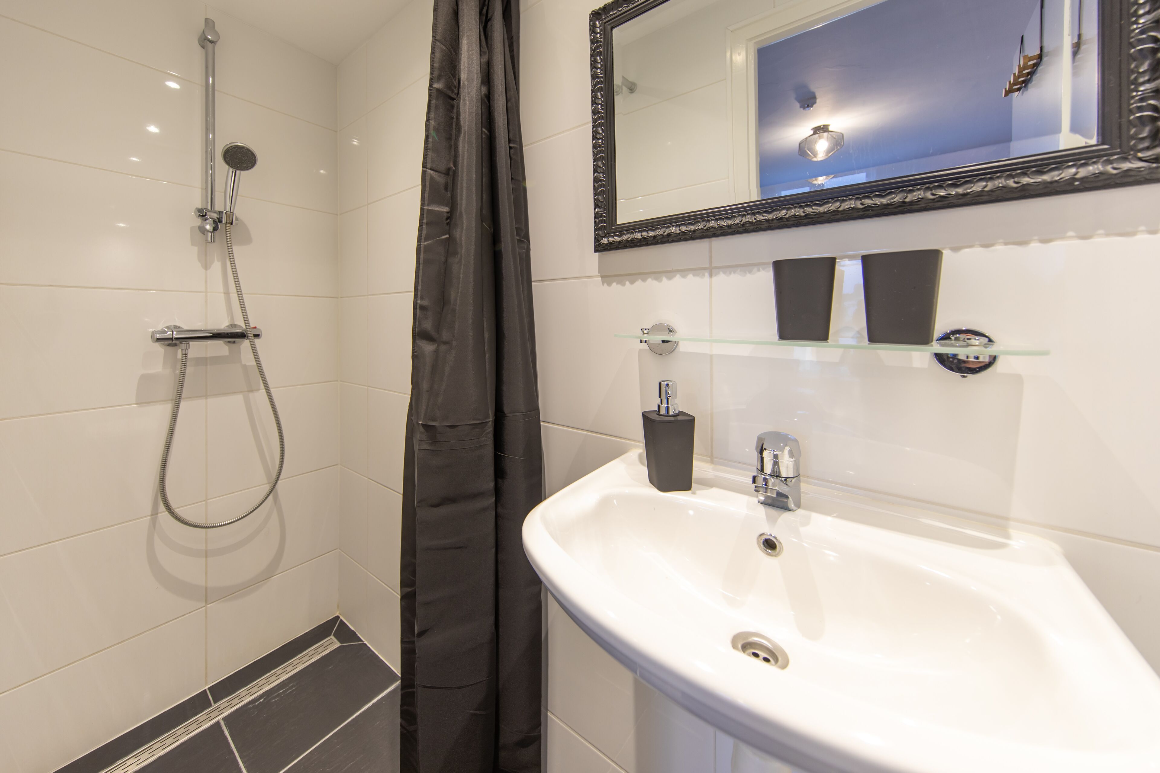 Un baño con ducha, lavamanos, espejo y estanterías.