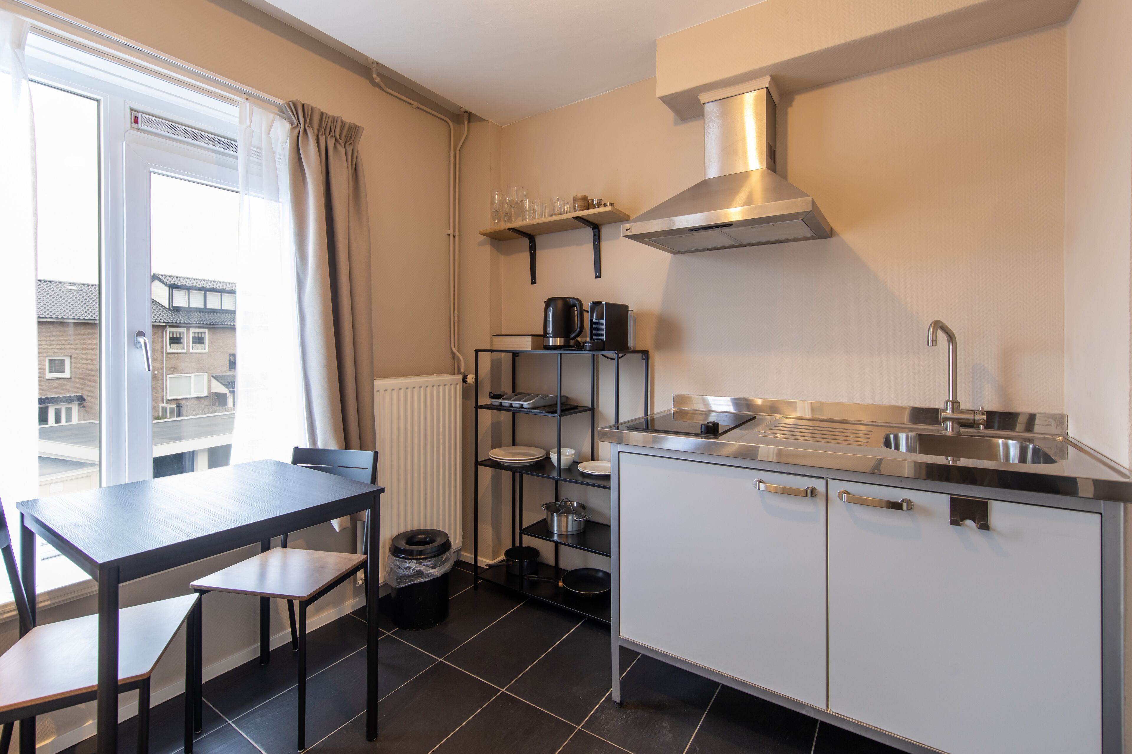 A compact kitchen with a dining table, a built-in oven, and a window with curtains.