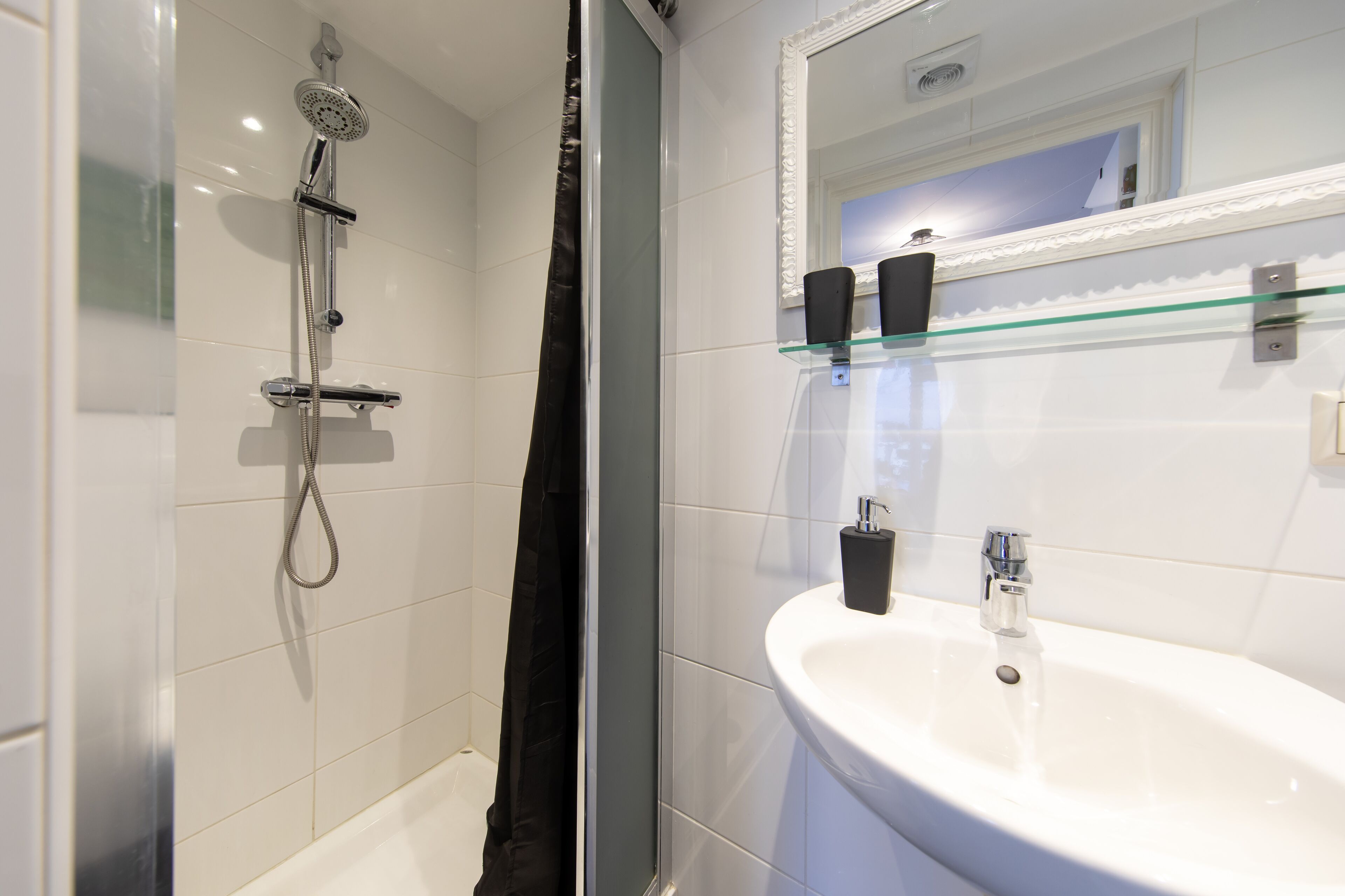 Et moderne badeværelse med en glasbrusekabine, en hvid vask og et spejl med dekorativ ramme.