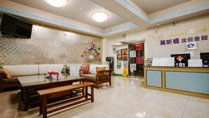 Un hall d’hôtel comprenant un comptoir d’accueil, un espace salon avec un canapé et des tables, des carreaux décoratifs sur les murs et un téléviseur à écran plat fixé au mur.