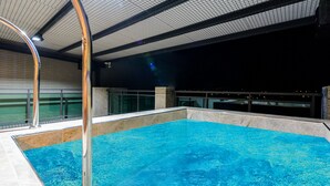 Une piscine intérieure à l’eau claire, entourée d’un sol et de murs carrelés, et dotée d’un escalier métallique.