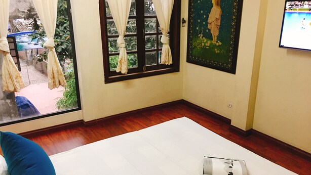Una habitación con un ventanal grande, una cama con almohadas azules, un cuadro en la pared y una pantalla de televisión mostrando un evento deportivo.