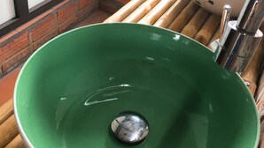 Un lavamanos verde de cerámica con grifo cromado, sobre un banco de madera con listones.