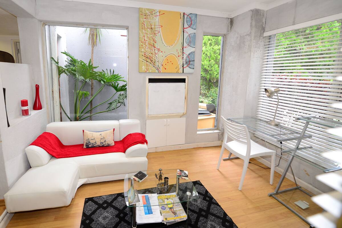 Una sala de estar moderna con un sofá blanco, una mesa de centro de vidrio y vistas al exterior con vegetación.