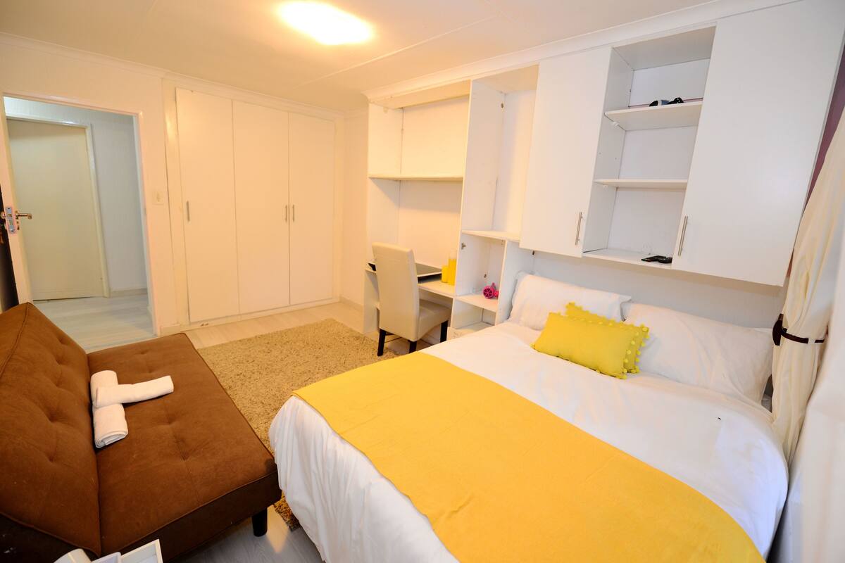 Una habitación de hotel con una cama, un sillón marrón, un escritorio y armarios empotrados.