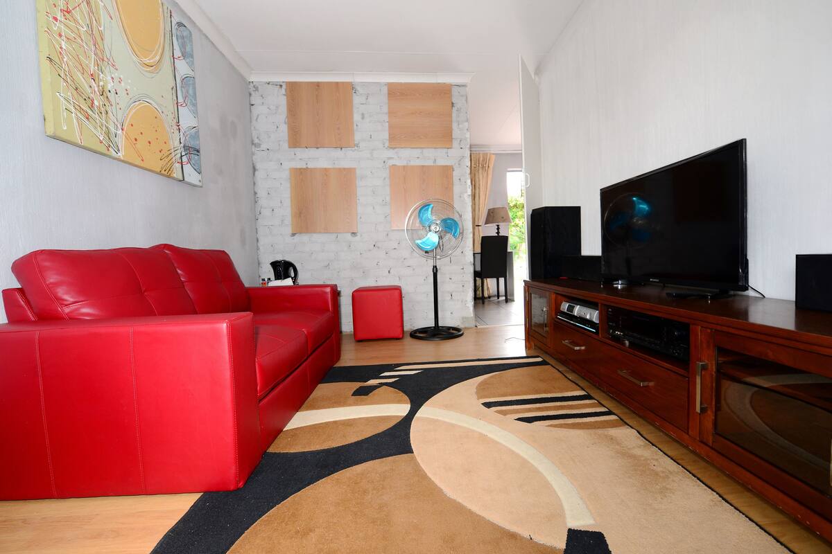 Una sala de estar con un sofá rojo, un mueble de madera para entretenimiento, un televisor de pantalla plana y una alfombra estampada.