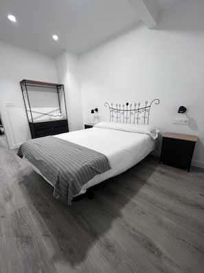 A modern bedroom with a bed, a bedside table, a nightstand, a wardrobe, and a wall-mounted lamp. - Hostal Mónaco (Valladolid)