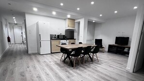 A modern kitchen with white cabinets, a wooden dining table, and recessed ceiling lights. - Hostal Mónaco (Valladolid)