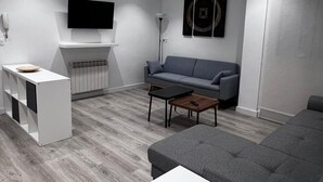 A modern living room with a grey sofa, a white entertainment unit, and a flat-screen TV mounted on the wall. - Hostal Mónaco (Valladolid)
