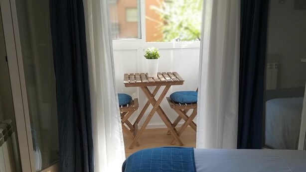 A bedroom with a bed, a small table with a potted plant, and a view of the outside. - Hostal Mónaco (Valladolid)