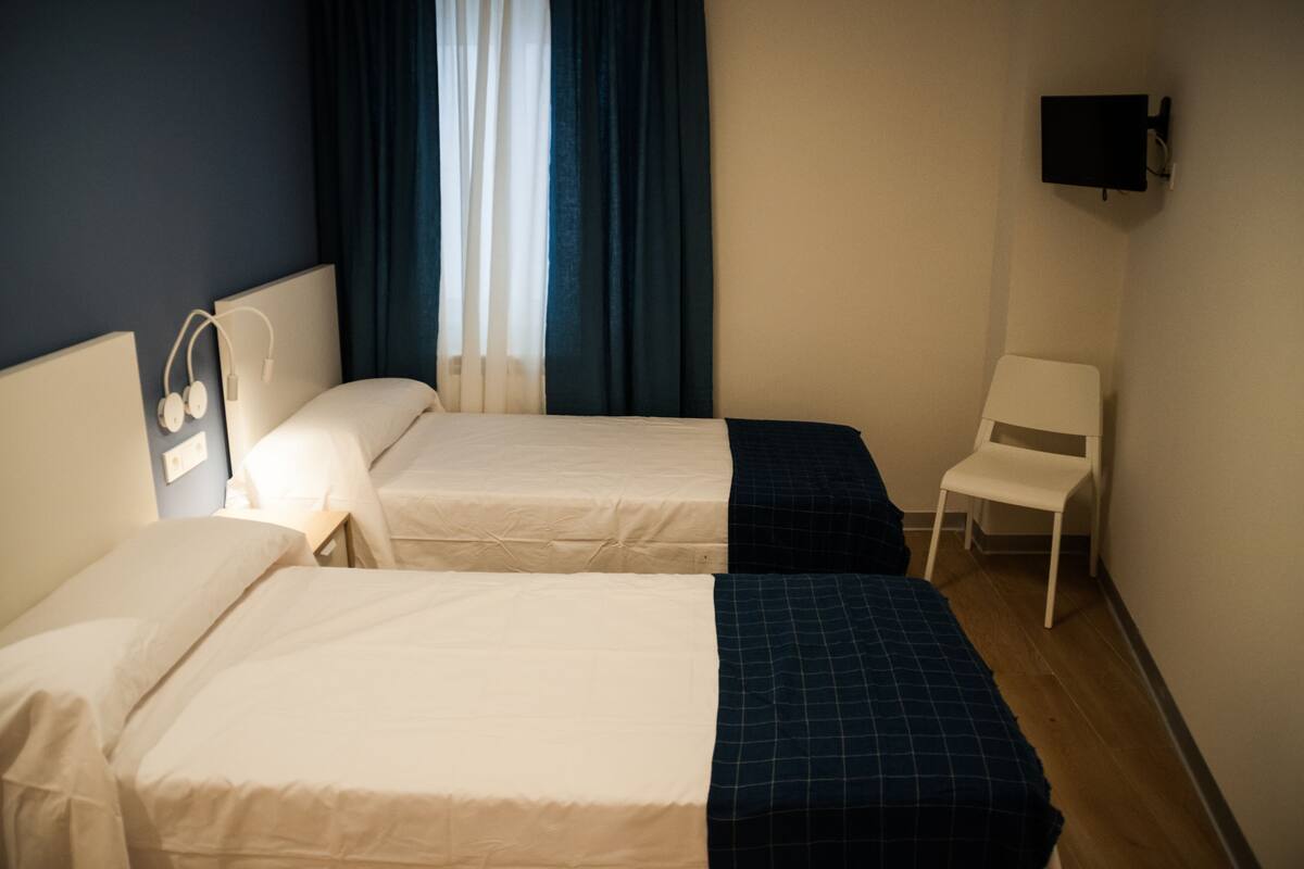 Habitación de hotel con dos camas, un televisor montado en la pared y una silla.