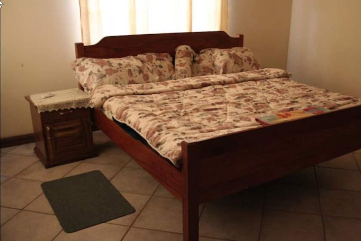 A bedroom with a wooden bed, floral bedding, a nightstand, and a small rug.
