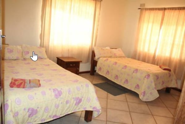 A hotel room with two beds, each with a floral bedspread, a nightstand, and a window with curtains.