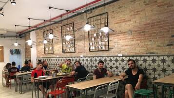 Un comedor con paredes de ladrillo, luces colgantes y sillas de metal. Las mesas están dispuestas para grupos.