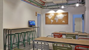 Un aula con un mapa mundial, una computadora y sillas verdes y rojas.