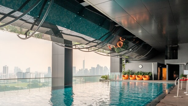Ein Innenpool mit Blick auf die Stadt, moderne Architektur und orangefarbene Pflanzgefäße am Rand.