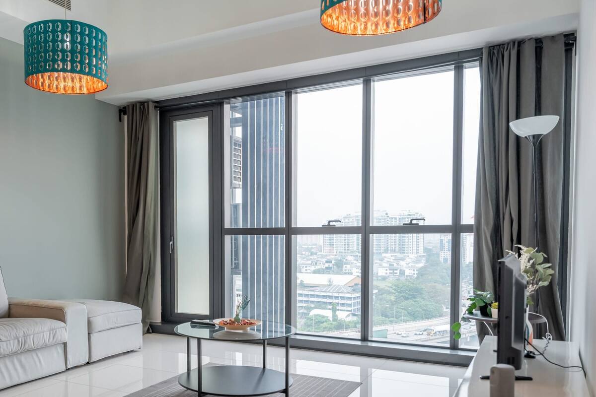 A modern living room with a sofa, a small table, and a large window offering a city view.