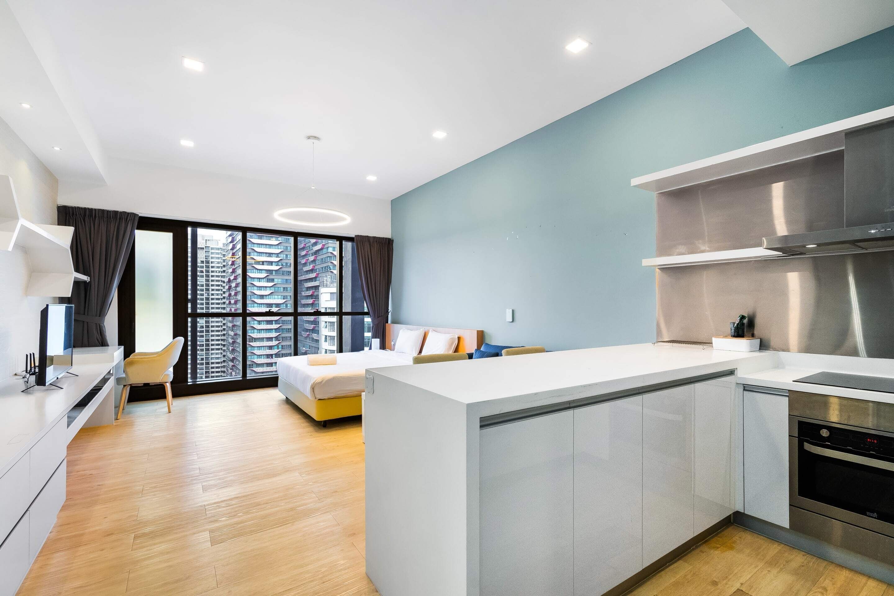 Een moderne hotelkamer met een groot bed, een kitchenette en uitzicht op hoge gebouwen.