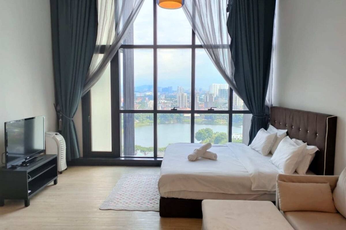 A hotel room with a large window, a bed, a TV, and a sofa.