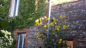 Un edificio rústico de piedra con muros cubiertos de hiedra y una ventana con barrotes blancos.