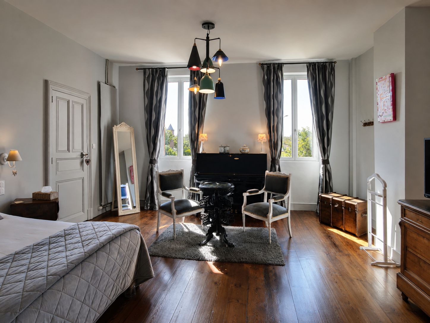 Un dormitorio con una cama, un piano, dos sillas, un espejo, un aparador y una televisión.