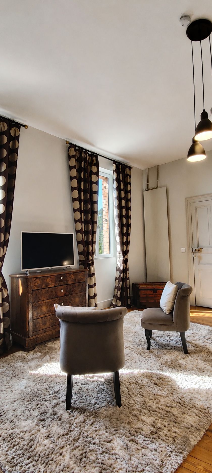 A living room with a flat-screen TV, two armchairs, a wooden cabinet, and a fluffy rug.