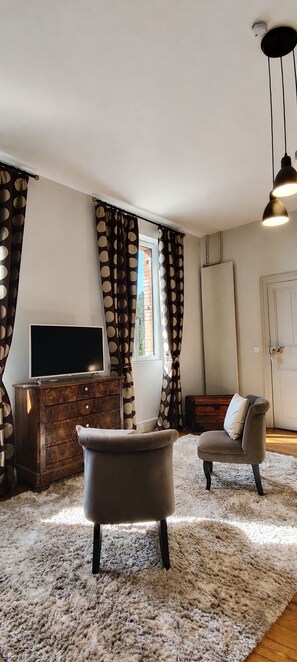 Un salón con televisor de pantalla plana, dos sillones, un aparador de madera y una alfombra mullida.