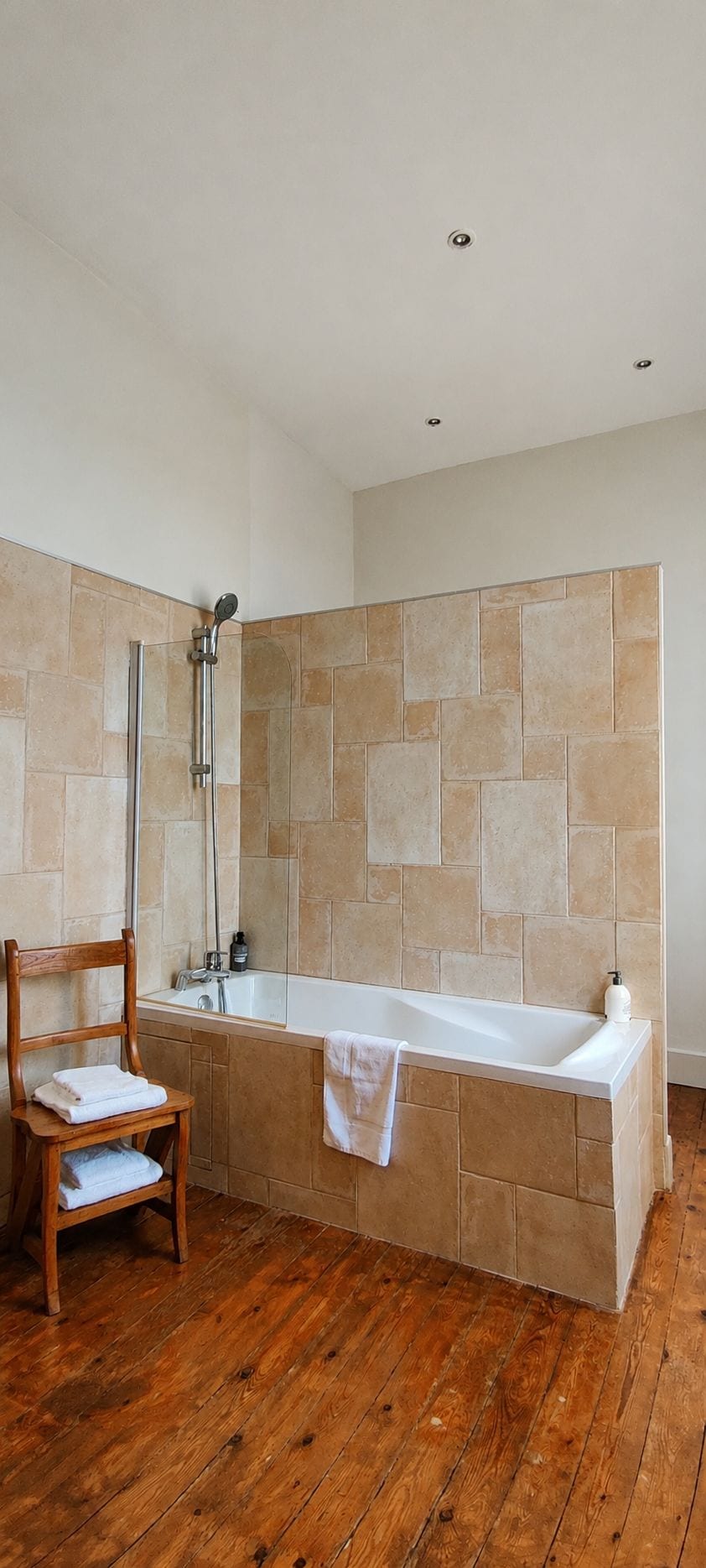 Une salle de bain avec une baignoire, une chaise en bois et une douche.