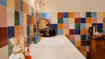 Una cocina con salpicadero de azulejos, un lavamanos, una cafetera y un armario de madera.