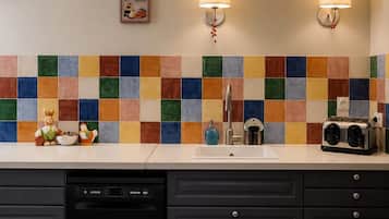 Una cocina con un salpicadero de azulejos coloridos, dos luces empotradas, un lavavajillas y una alfombra con motivos de café.