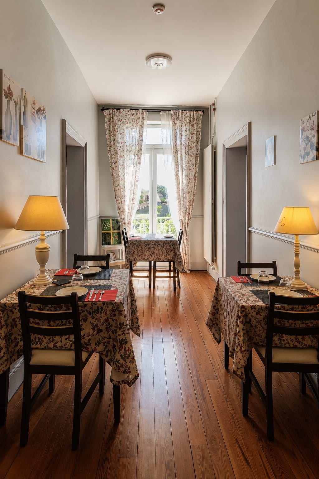 A dining area with two tables, each with a floral tablecloth, chairs, and lamps.