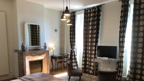 Habitación de hotel con una cama, un escritorio con televisor, una silla, chimenea y cortinas a lunares.