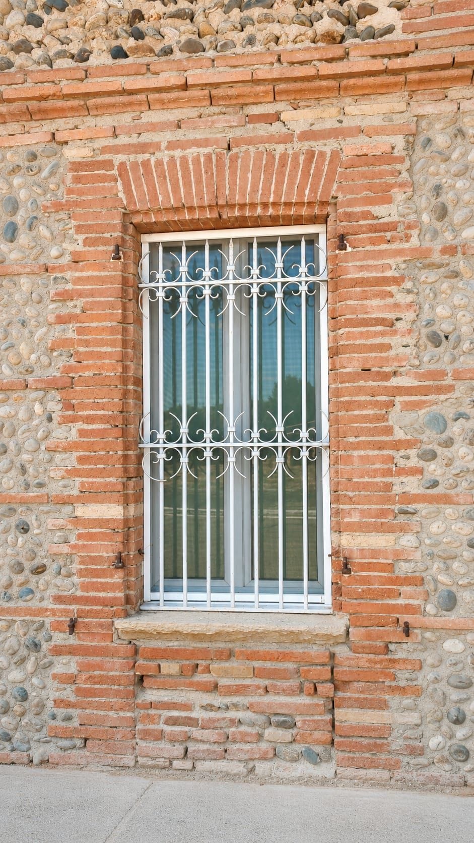 A window with ornate metal bars, set in a brick wall with a stone base.