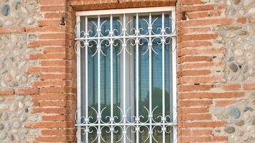 A window with ornate metal bars, set in a brick wall with a stone base.