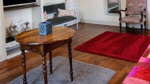 A room with a wooden table, a red rug, a patterned chair, a mirror, and a television. -  Maison de Maître Gentil'Home - 1699 (Fenouillet)