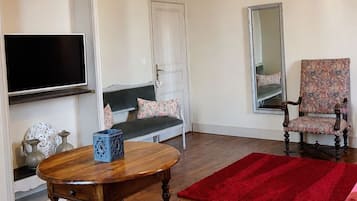 Een kamer met een houten tafel, een rood tapijt, een gestreept fauteuil, een spiegel en een televisie.