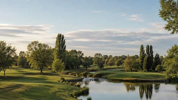 Un parcours de golf paisible, agrémenté d’un étang, d’arbres et d’un ciel dégagé.