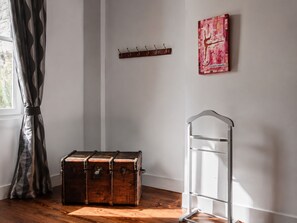 A room with a wooden floor, a vintage trunk, a metal shelf with hooks, and a painting on the wall. - Maison de Maître Gentil'Home - 1699 (Fenouillet)