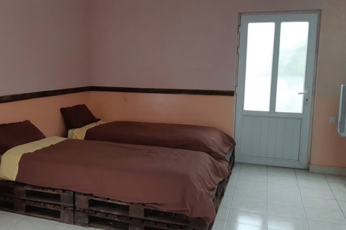 A bedroom with two beds, a wooden dresser, a door, and a television.