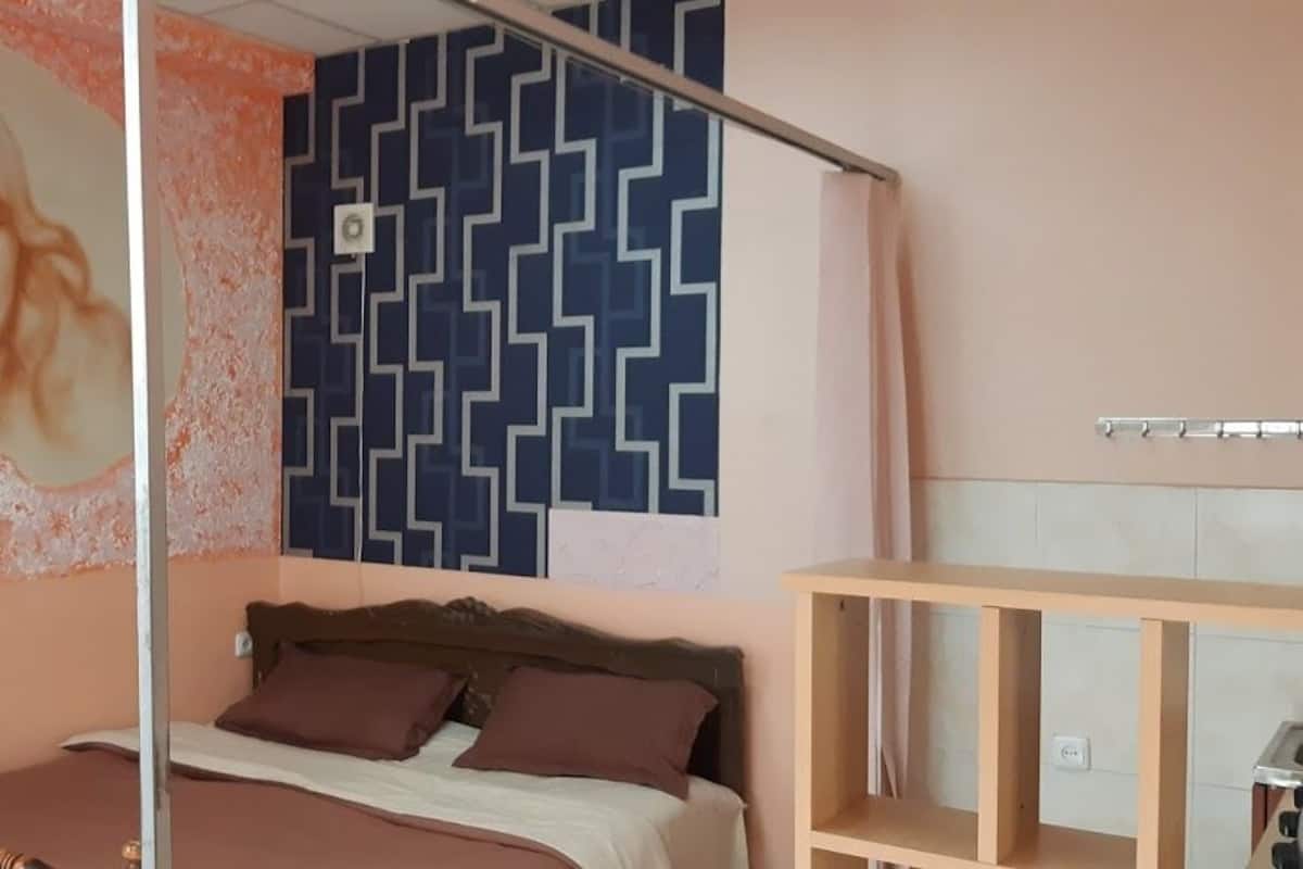 A bedroom with a bed, a headboard, a wall with a geometric pattern, and a shelf unit.