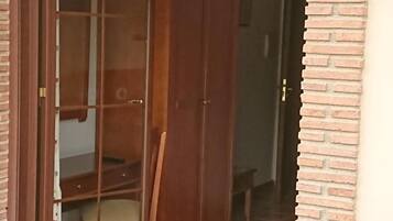 Una puerta corrediza de vidrio da acceso a una habitación con un armario de madera y suelo de baldosas.