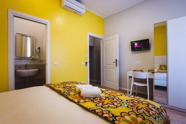Une chambre d’hôtel équipée d’un lit, d’un bureau, d’une chaise, d’un lavabo et d’une télévision.