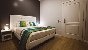 A bedroom with a white bed, a nightstand with a lamp, and a door.