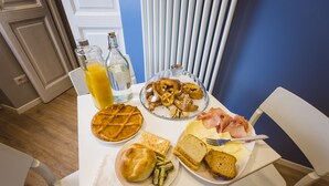 A breakfast table with various food items, including pastries, bread, cheese, and ham, along with a bottle of orange juice and a glass of water.