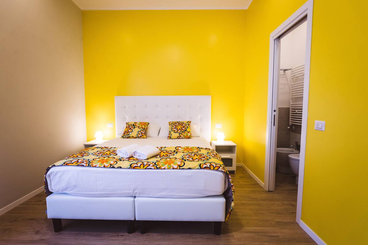 A bedroom with a bed, bedside tables, and a bathroom visible through an open door.