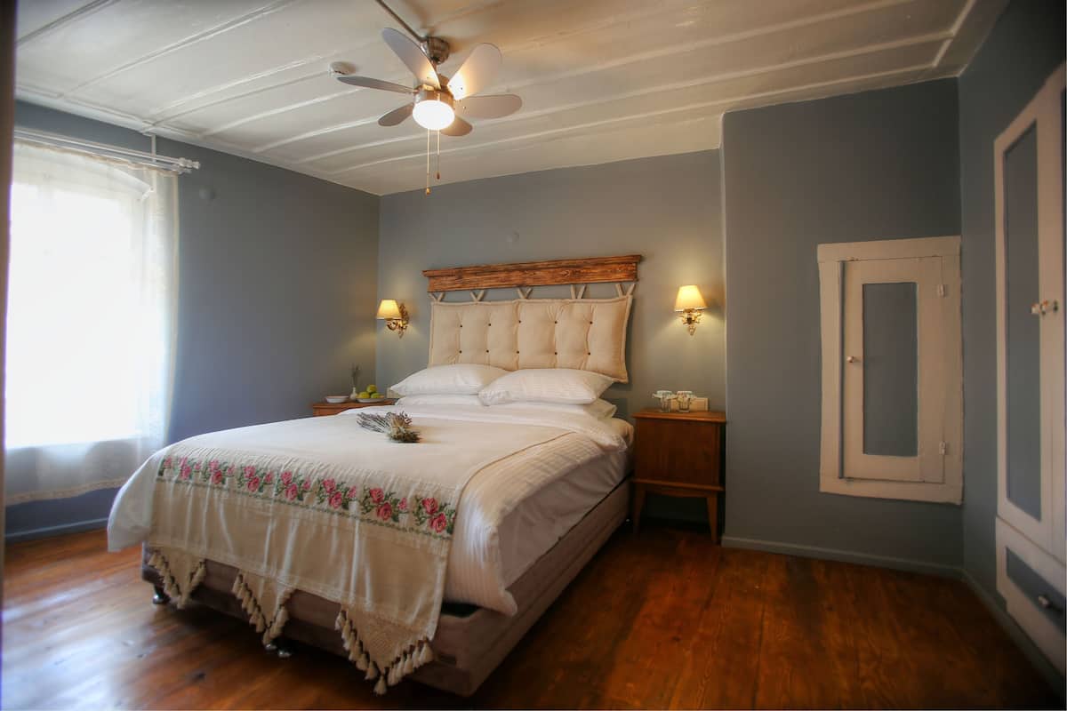 A bedroom with a wooden bed, a ceiling fan, two bedside lamps, and a window with curtains.