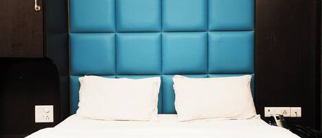 Ein Bett mit blauem Kopfteil, weißer Bettwäsche und einem Nachttisch mit Telefon und Ladegerät.