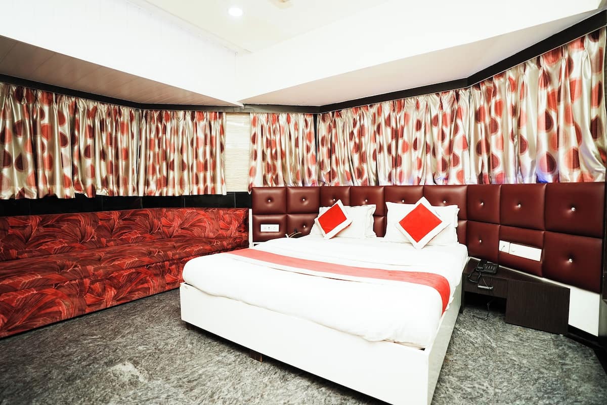 Una habitación de hotel con una cama grande, un papel tapiz rojo y blanco estampado y una ventana con cortinas.