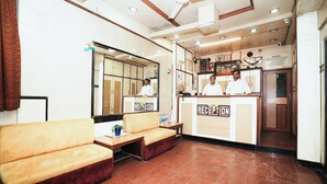 A reception area with a sofa, a reception desk, and a mirror. - Hotel Kings Palace (Mumbai)