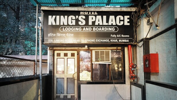 Entrada de un hotel con un letrero que dice "KING'S PALACE Alojamiento y Pensión" y menciona "Habitaciones con aire acondicionado completo" en 538 Linking Road, cerca de la central telefónica, Khar, Mumbai.